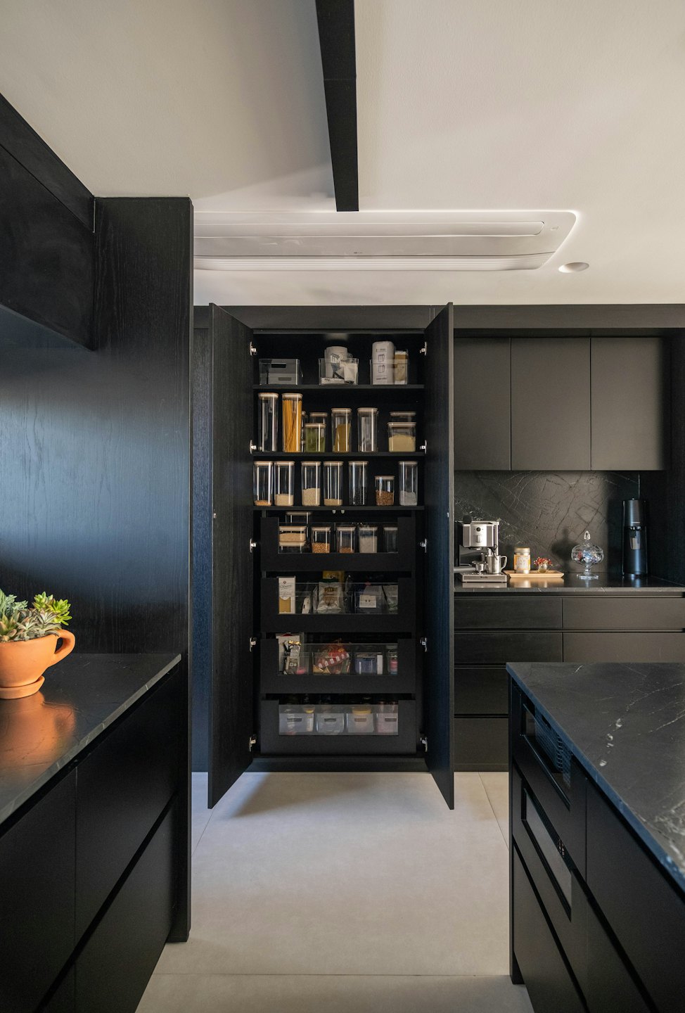 Organized pantry shelves and kitchen appliances on dark countertops.